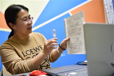 妻子王之玲拿著教材，在電腦前上初三物理課。